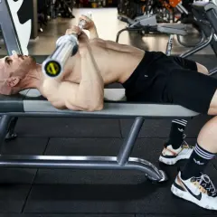 Uomo calvo si allena in palestra, sollevando un bilanciere su una panca. Un esempio di **super serie palestra** per un allenamento intenso.