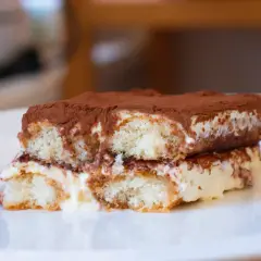 Ein Stück original italienisches Tiramisu, üppig mit Kakao bestäubt, auf einem weißen Teller.