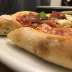 Nahaufnahme einer köstlichen Pizza mit dickem, luftigem Rand, belegt mit Tomaten, Käse und Salami. Ein echter Genuss, wie ein kleiner "pizza canotto".