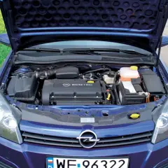Silnik Ecotec w niebieskim Opel Astra H 1.6 benzyna, z otwartą maską, na tle pola rzepaku.