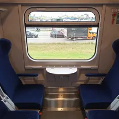 Wnętrze wagonu 174a z niebieskimi siedzeniami i oknem, przez które widać drogę z samochodami i ciężarówką.