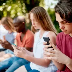 Grupa nastolatków siedzi na ławce, każdy pochłonięty smartfonem. Warto zadbać o ich bezpieczeństwo online, np. poprzez kontrolę rodzicielską na Androidzie.