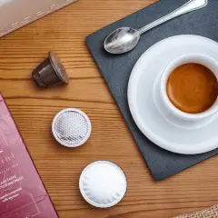 Una tazzina di espresso fumante, capsule e confezione Rossini: un invito a gustare una nota varietà di caffè.