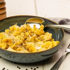 Eine Schüssel Pasta mit cremiger cacio e pepe sauce, bestreut mit frisch gemahlenem Pfeffer. Daneben liegen ein Löffel und eine Gabel.