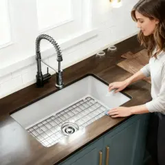 A woman cleans the edge of a new undermount sink installation. The stainless steel sink has a grid rack and a modern black faucet.