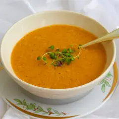 En skål med varm, orange turkisk linssoppa, garnerad med färska örter och en elegant sked.