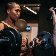 Zwei Männer trainieren im Fitnessstudio. Der vordere Mann hebt eine Hantel, der hintere Mann stemmt eine Kurzhantel. Verschiedene Kraft Arten werden hier gezeigt.