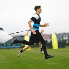 Młodzi sportowcy trenują bieganie z paralotnią, ćwicząc koordynację i siłę.
