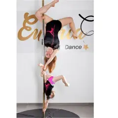 Dwie dziewczyny ćwiczą pole dance. Młodsza wspiera starszą, która wisi głową w dół.