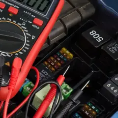 A multimeter is used to test a car's fuse box and relays.