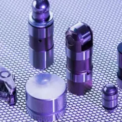 Varios taques hidráulicos de metal, algunos con forma cilíndrica y otros con un diseño más complejo, dispuestos sobre una superficie texturizada.