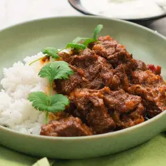 A bowl of lamb curry with rice and cilantro garnish.