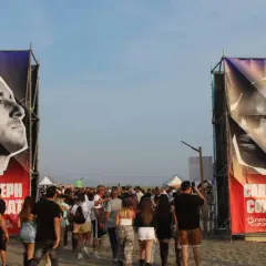Ingresso per il festival con gigantografie di Carl Cox e Joseph Capriati. La folla si muove sulla sabbia.