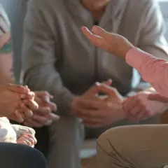 Grupa ludzi siedzi w kręgu, słuchając mówcy. To przykład socjoterapii, która pomaga w budowaniu relacji i wsparciu.