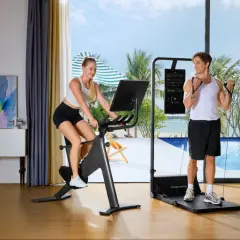 Ein Paar macht Ausdauertraining zuhause: Sie auf dem Fahrrad, er mit Widerstandsbändern. Der Blick geht auf ein tropisches Paradies.