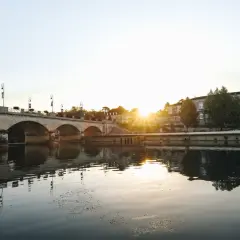 Un pont de pierre traverse une rivière calme, reflétant le soleil couchant sur les bâtiments historiques. Une belle vue pour savoir quoi faire à Cognac.