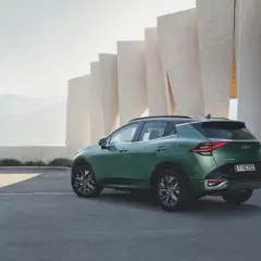 Zielony samochód Kia Sportage zaparkowany przed nowoczesnym budynkiem z elementami skalnymi w tle.