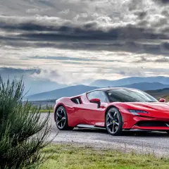 Czerwone Ferrari SF90 na tle gór i burzowego nieba.