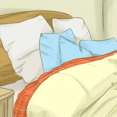 Cozy bed with pillows and a plaid blanket, perfect for learning how to get warmer in bed.