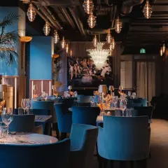 Elegant pava restaurang med blå sammetsstolar, marmorbord och dekorativa lampor.