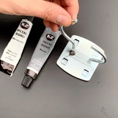 Dwie tubki kleju do blachy K2 Metal Bond (żywica i utwardzacz) oraz metalowy element z nałożonym klejem.