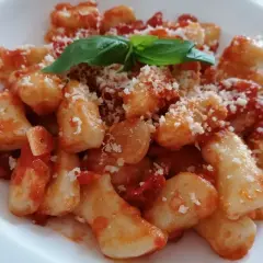 Pyszne gnocchi z sosem pomidorowym, posypane parmezanem i udekorowane listkiem bazylii.