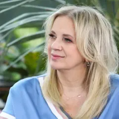 Marzena Rogalska w błękitnej bluzce z naszyjnikiem, na tle zieleni.