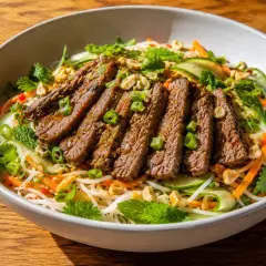 En skål med asiatisk biffsallad med nudlar, strimlad biff, gurka, morötter, mynta och jordnötter.