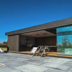 Nowoczesna altana przy domu z kuchnią letnią, miejscem do siedzenia i placem zabaw dla dzieci.