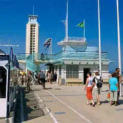 Promenade de Malo-les-Bains avec tramway, tour, bâtiments bleus et baigneurs sur la plage.