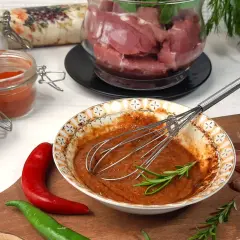 Przygotowanie marynaty do polędwiczki wieprzowej: miska z przyprawami, chili, czosnek i mięso w tle.