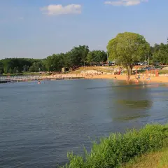 Słoneczny dzień nad zalewem Siemiatycze. Ludzie odpoczywają na piaszczystej plaży, niektórzy kąpią się w wodzie.