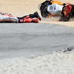 Piloto de MotoGP en el suelo tras una caída. La moto, volcada, derrapa en la grava. Un largo lap de competición que terminó mal.