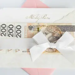 Elegancka koperta z banknotami 200 zł, przewiązana białą wstążką. Idealny prezent ślubny, który może być opodatkowany.