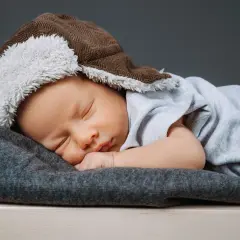 Słodki noworodek śpi w ciepłej, brązowej czapeczce z białym futerkiem, idealnej jako czapeczka dla noworodka do szpitala.