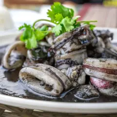 Calamares en su tinta, un plato oscuro y delicioso, adornado con cilantro fresco.