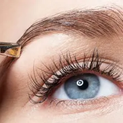 Une pince à épiler ajuste un sourcil. Un geste simple pour un dessin sourcil facile et un regard parfait.