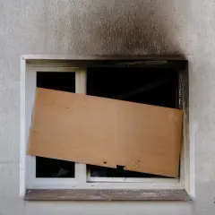 Beschädigtes Fenster, provisorisch mit Holzplatte verschlossen. Die Frage, wie lange bleibt eine Wohnung versiegelt, bleibt offen.