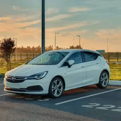 Biała Opel Astra K zaparkowana na parkingu. Słońce zachodzi, tworząc ciepłą atmosferę. Czas na opel astra k wymiana akumulatora.