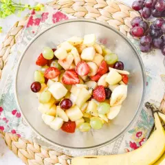 Un tazón lleno de colorida ensalada de frutas con fresas, uvas, plátano y trozos de manzana.