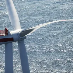 Ogromna turbina wiatrowa na morzu, symbol nowoczesnej morskiej energetyki wiatrowej, obraca łopatami na tle błyszczącej wody.