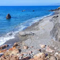 Costa de Almería, con sus guainos y rocas, el mar azul y las olas rompiendo en la playa de guijarros.
