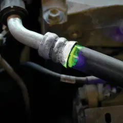 Detectando una fuga de aire en el sistema de aire acondicionado con tinte fluorescente verde y luz ultravioleta.