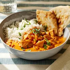 Miseczka z ryżem i kurczakiem w kremowym sosie butter masala, ozdobiona natką pietruszki, podana z chlebkiem naan.