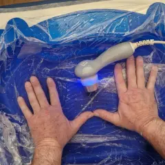 Mani immerse in un bagno blu per ultrasuoni in acqua per piedi, con un manipolo che emette luce blu.