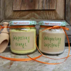Zwei Gläser mit selbstgemachtem Saunasalz (Orange & Grapefruit) und eine Holzschaufel, verziert mit orangefarbenen Bändern.