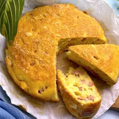 Torta salata prosciutto e formaggio dorata, con una fetta tagliata, su carta forno.