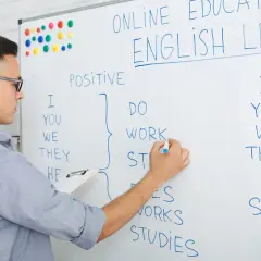 Chłopak pisze na tablicy "ONLINE ENGLISH LESSON". Uczy się, ile jest słów w języku angielskim, tworząc zdania.