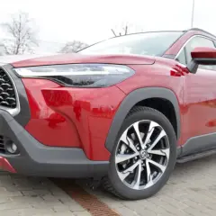 Czerwona Toyota Corolla Cross na zdjęciu prezentuje się imponująco, a jej wysoki prześwit sugeruje gotowość do pokonywania różnych dróg.