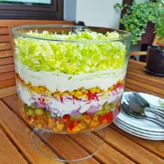Warstwowa sałatka gyros, tradycyjny przepis. Widoczne mięso, warzywa, kukurydza, sos i sałata lodowa w szklanej misie.